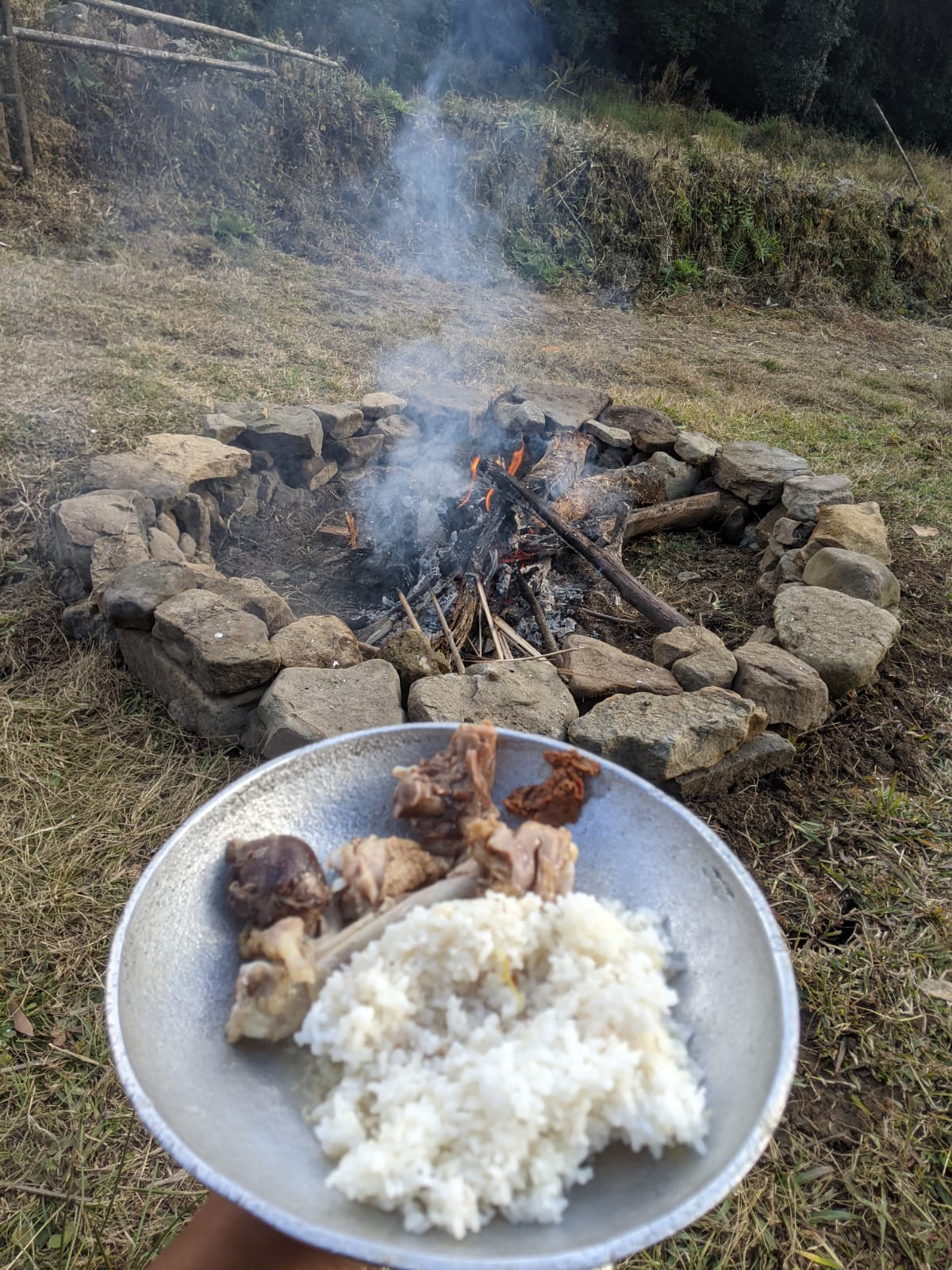 A plate of rice and smoked meat beside an outdoor fire in Dzüleke