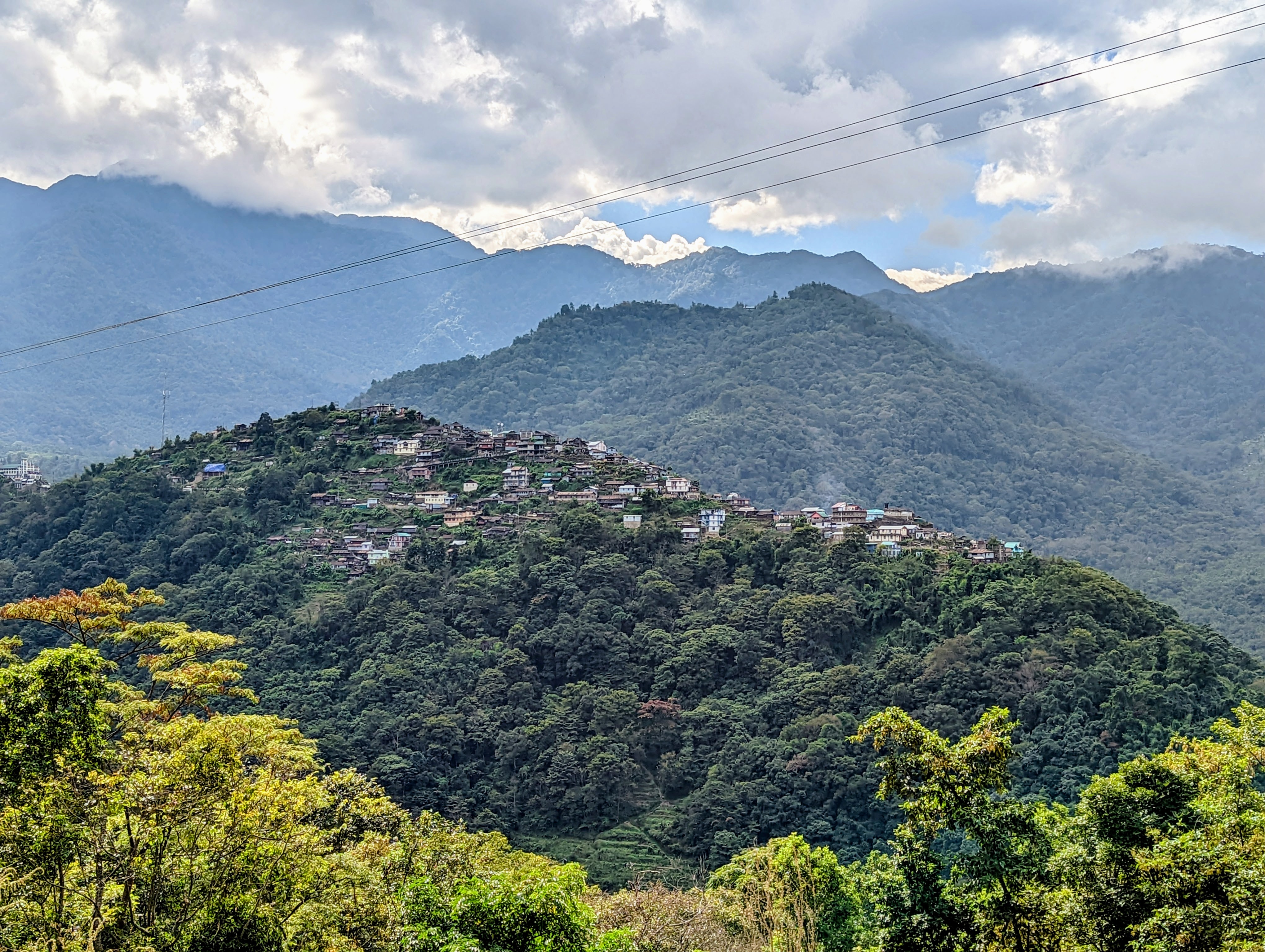 A hilltop village seen from the road to Dzüleke, with layered mountains and clouds behind